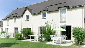 A row of white buildings with a flat roof and multiple windows. There are outdoor seating areas with white tables and chairs, and a green umbrella. - Les Jardins Renaissance by Interhome (Azay-le-Rideau)