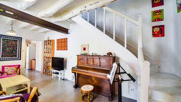 Een ruime woonkamer met een piano, een televisie en een trap.