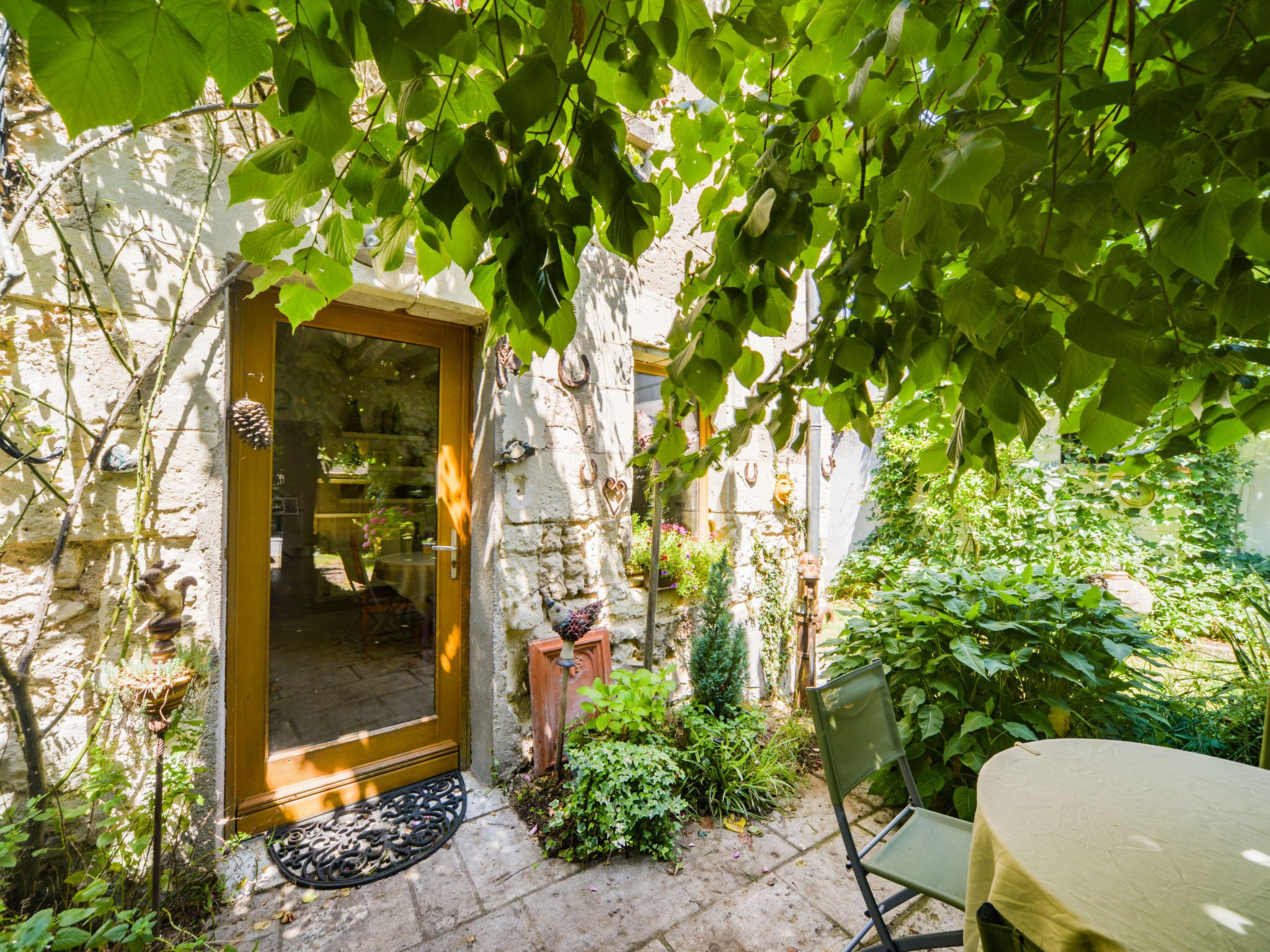Un bâtiment en pierre avec une porte en bois, un petit espace jardin avec une chaise et une table, et une plante en pot.
