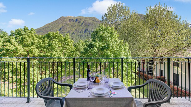 A table set outdoors with a mountain view, a balcony railing, and chairs. - Porto Letizia Napoli 8, Porlezza, Italy (Porlezza)