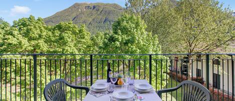 A table set outdoors with a mountain view, a balcony railing, and chairs.
