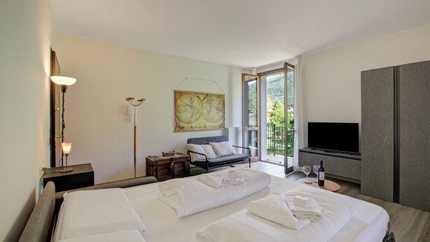 A hotel room with a large bed, a sofa, a TV, and a balcony with a view. - Porto Letizia Napoli 8, Porlezza, Italy (Porlezza)