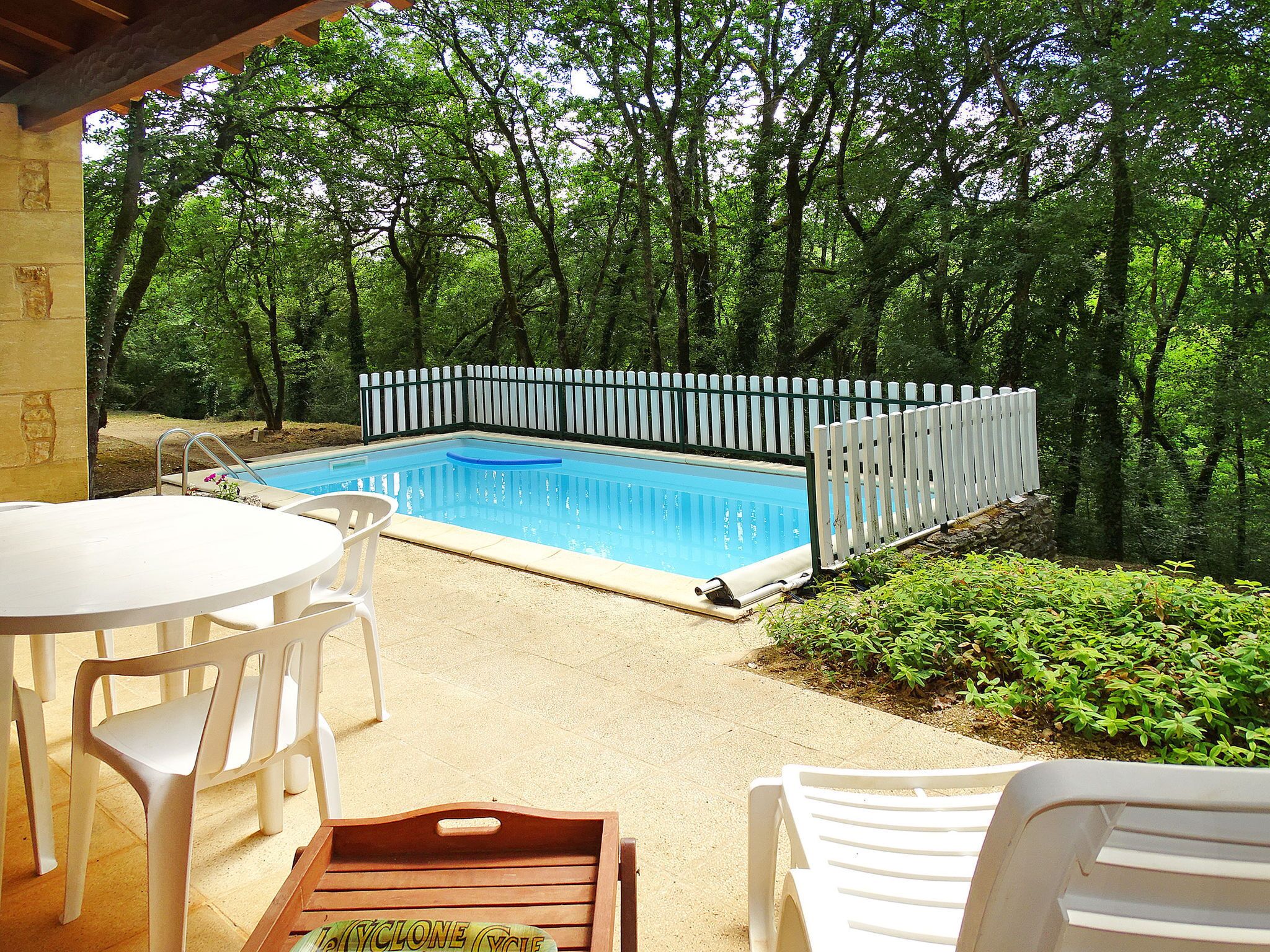 A swimming pool with a white fence, surrounded by greenery and trees.