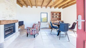 A cozy living room with a fireplace, a dining area with a table and chairs, and a view through a window. - Vacation home Cuzac by Interhome (Labastide-Murat)