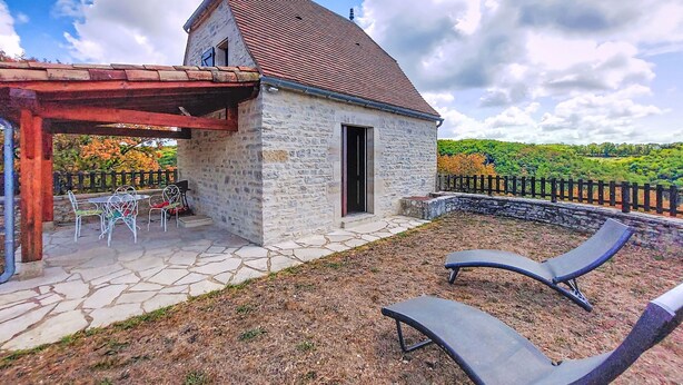A stone building with a tiled roof, a covered patio with chairs, and a view of a hilly landscape. - Vacation home Cuzac by Interhome (Labastide-Murat)
