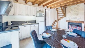 A modern kitchen with white cabinets, a built-in microwave, and a dining area with a marble table and blue chairs. - Vacation home Cuzac by Interhome (Labastide-Murat)