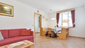 Un salon chaleureux avec un canapé rouge, une table à manger en bois et des chaises, ainsi qu’une fenêtre avec des rideaux.