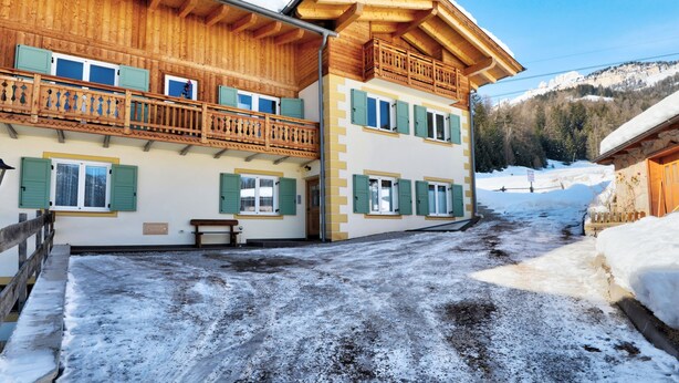 Un chalet en bois à deux étages, doté de balcons et d’une terrasse en bois, et surplombant un paysage enneigé.