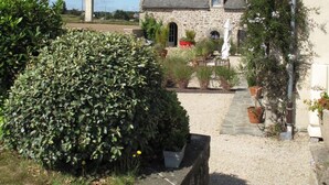 A stone house with a gravel driveway, surrounded by greenery and potted plants.