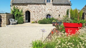 A stone building with a gravel driveway, a white chair, and various plants.