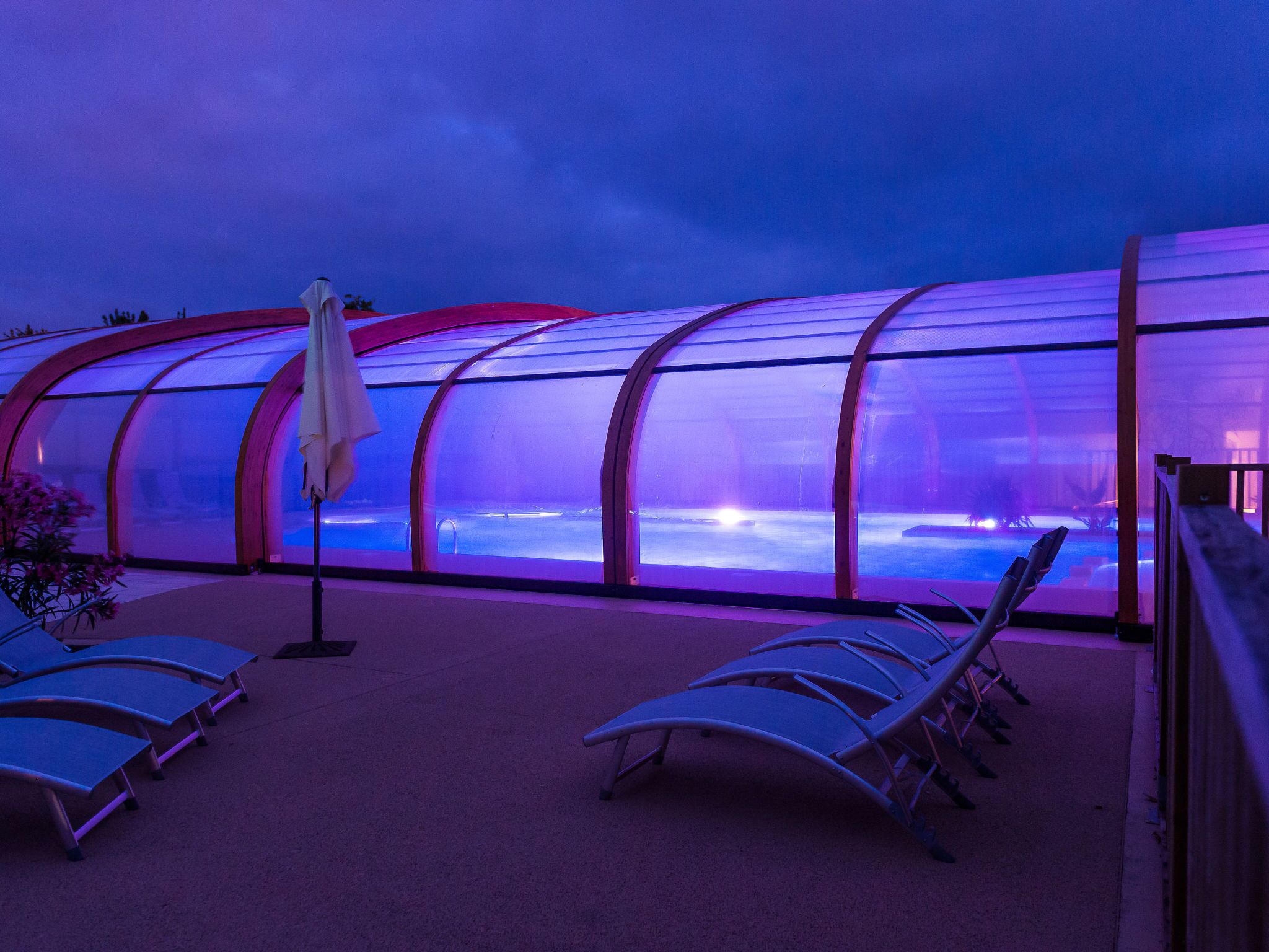A greenhouse structure with transparent walls, a seating area with lounge chairs, and a small table with an umbrella.