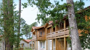 A wooden cabin-style building with a balcony, surrounded by trees and a well-maintained lawn.