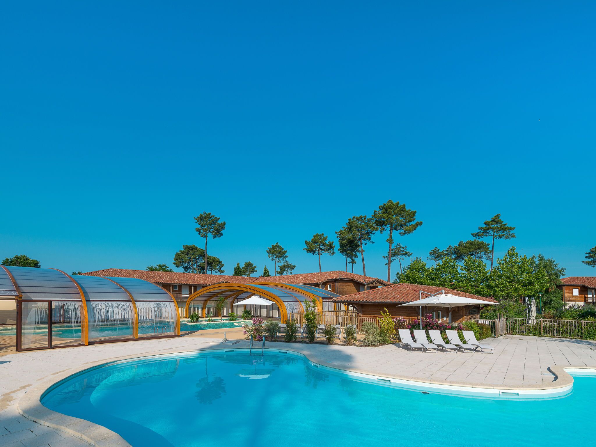 Una piscina con lettini da relax e una zona ombreggiata, circondata da alberi ed edifici.