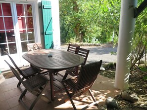 An outdoor patio with a round table and four chairs, surrounded by a white column and greenery.
