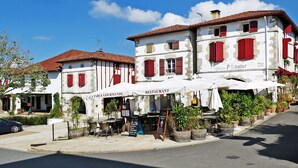 Un restaurante con terraza, fachada blanca, contraventanas rojas y un letrero que dice 'LA TABLE GOURMANDE RESTAURANT'.