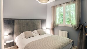 A bedroom with a bed, bedside tables, a window with curtains, and a radiator. - Collines Iduki by Interhome (La Bastide Clairence)