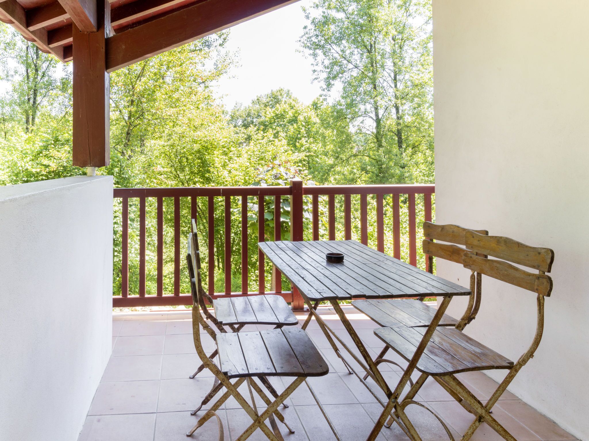 A wooden table and bench on a balcony with a red railing, overlooking a forested area.