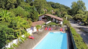 Una piscina con sillas de descanso, rodeada de exuberante vegetación y un edificio de techo rojo.
