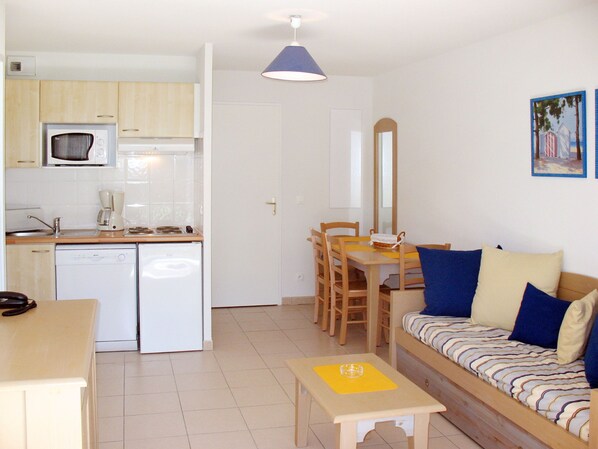 Un espacio habitable compacto con kitchenette, comedor y sofá con cojines.