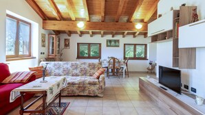 Un salon spacieux avec un haut plafond en bois, un canapé rouge, un canapé à motifs floraux, une table à manger avec des chaises et un téléviseur posé sur un meuble en bois.