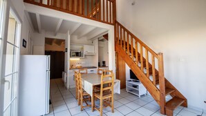 A spacious kitchen with a dining area, wooden staircase, and white tiled flooring. - Résidence Dune Blanche - Soleil by Interhome (Biscarrosse)