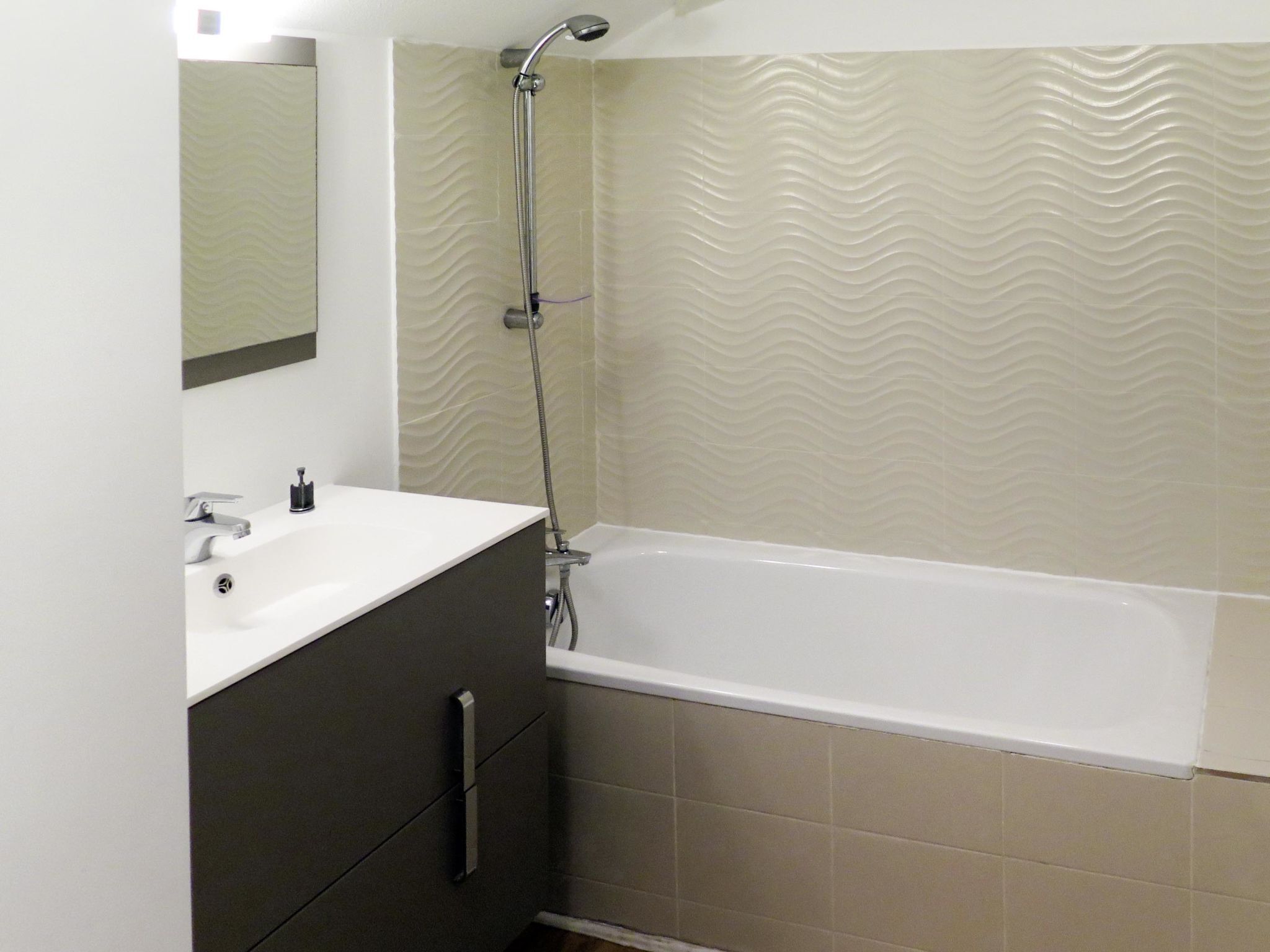 Ein Badezimmer mit Waschbecken, dunklem Schrank und einer Badewanne mit Duschkopf.