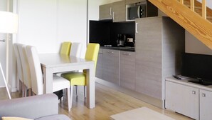 A modern living space with a sofa, a dining table with chairs, a kitchen area with a microwave, and a TV on a cabinet. - Les Balcons de l’Océan by Interhome (Biscarrosse)