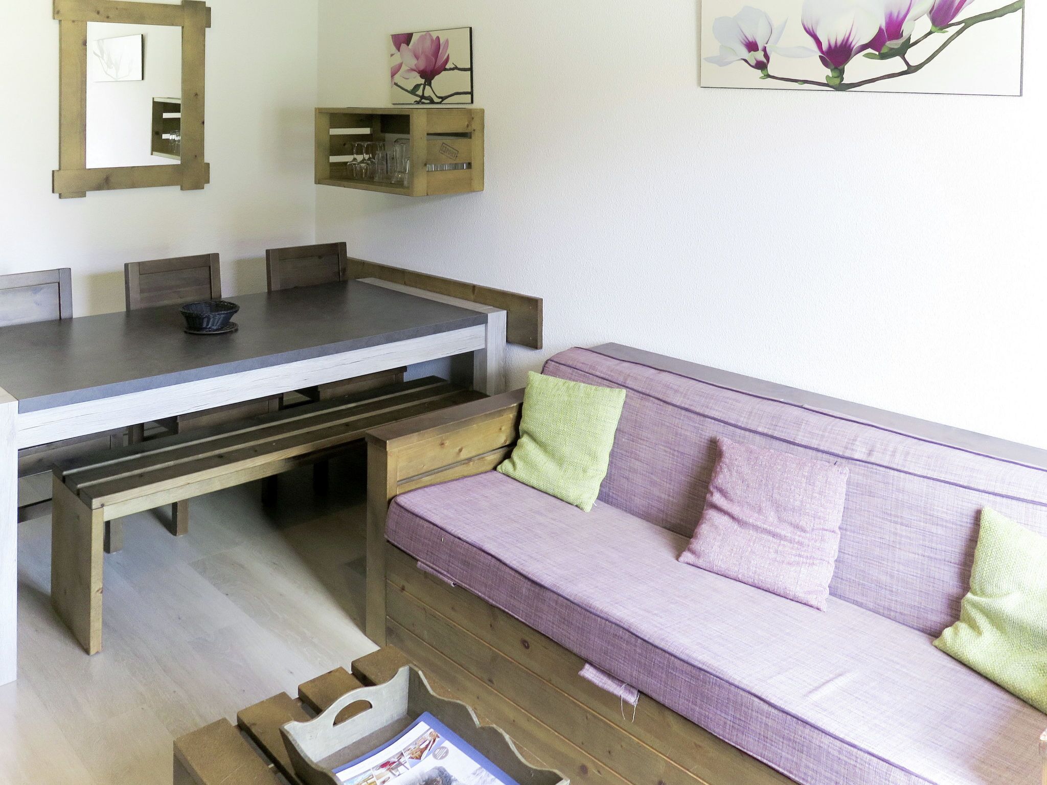A living room with a wooden dining table, a purple sofa, and a wooden bench.