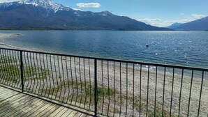 A lakeside view with mountains in the background, a wooden deck, and a metal railing.