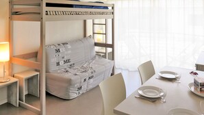 A bunk bed with a sofa, a dining table with plates and glasses, and a lamp. - Résidence Plage Centrale T2 by Interhome (Hossegor)