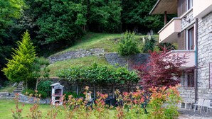 Ein Steinhaus mit einem Garten davor, einem kleinen Gazebo und einem bewaldeten Hügel.
