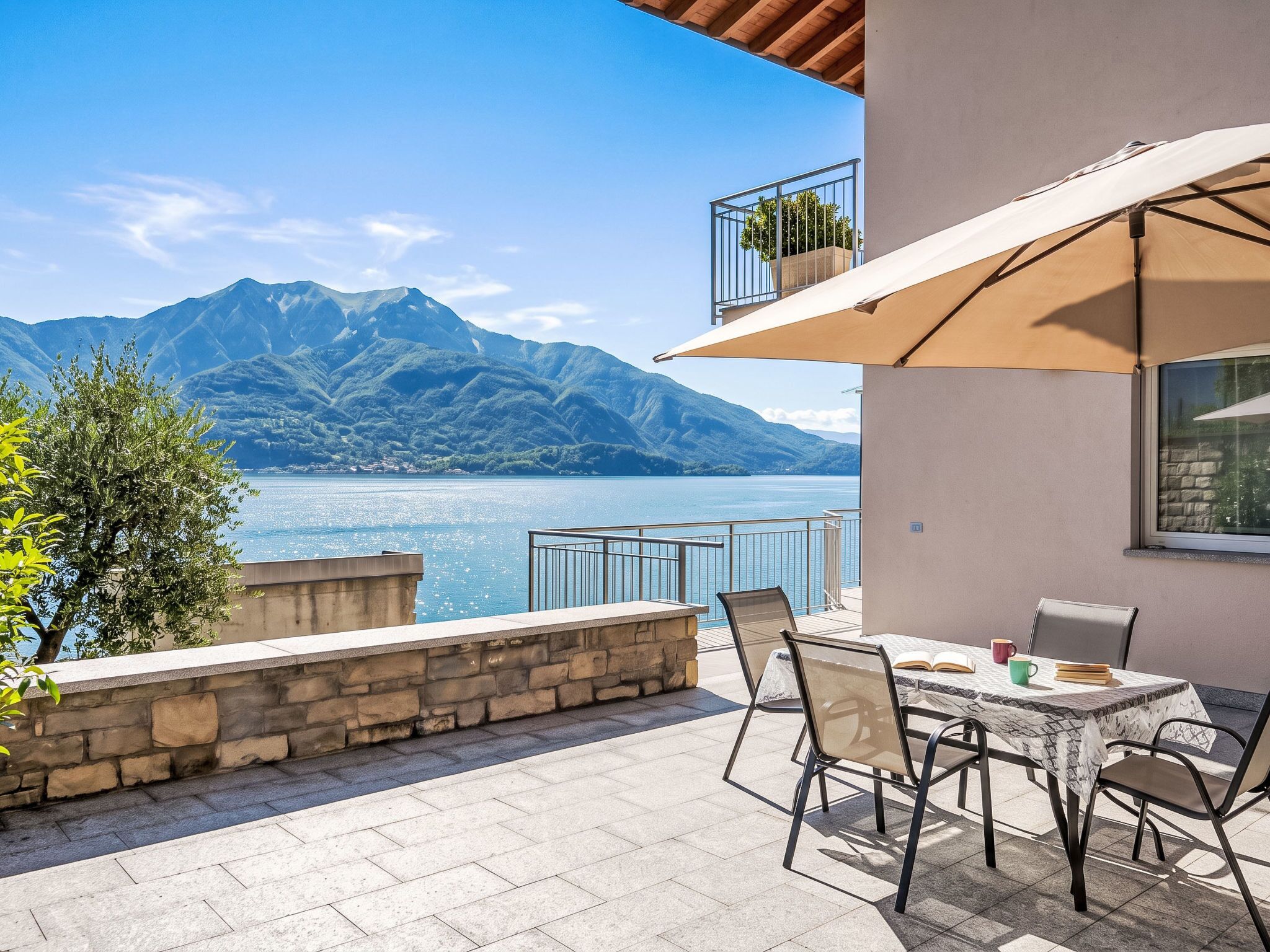A terrace with a table and chairs, overlooking a lake and mountains.