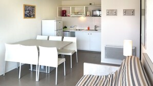 Una habitación de hotel compacta con mesa de comedor, sillas, cama con ropa de cama a rayas, kitchenette y un baño pequeño.