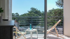 Un balcón con una mesa, sillas, una planta en maceta y vistas a árboles y edificios.