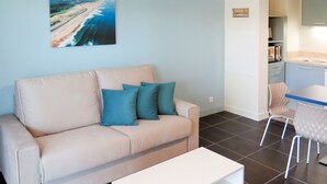 Een moderne woonkamer met een beige bank, een witte salontafel en een schilderij van een blauwe uitzicht op de oceaan aan de muur.