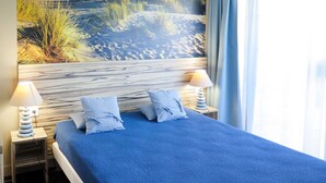 Een hotelkamer met een bed, twee bedlampen en een groot raam met gordijnen.