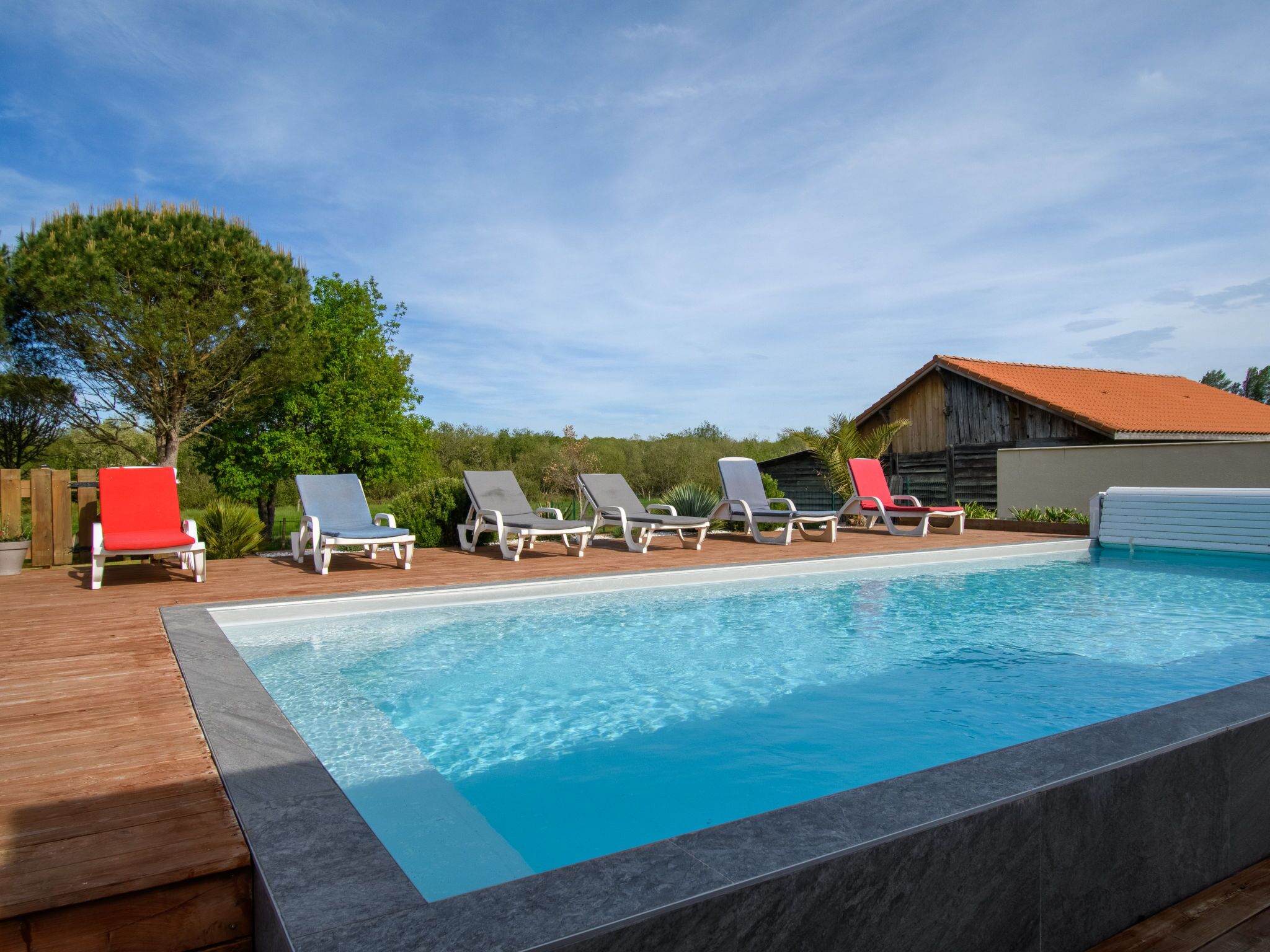 A swimming pool with six lounge chairs, a wooden deck, and a rustic building in the background.
