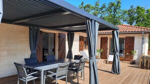 An outdoor patio with a covered table and chairs, wooden flooring, and a view of the surrounding area. - Petrocq by Interhome (Lit-et-Mixe)