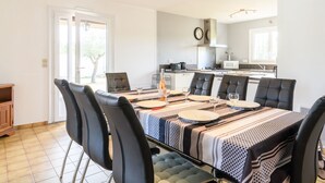 A dining area with a table set for six, surrounded by black chairs, in a modern kitchen with white cabinets and a visible clock. - Petrocq by Interhome (Lit-et-Mixe)