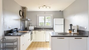 A modern kitchen with white cabinets, a stainless steel range hood, a microwave, a refrigerator, and a coffee maker. - Petrocq by Interhome (Lit-et-Mixe)