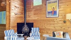 A cozy cabin interior with a wood-burning stove, striped chairs, a sofa, and a poster on the wall. - L'Escouarte by Interhome (Maubuisson)