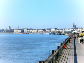 A riverside promenade with a view of a city skyline, including historic buildings and a cathedral.