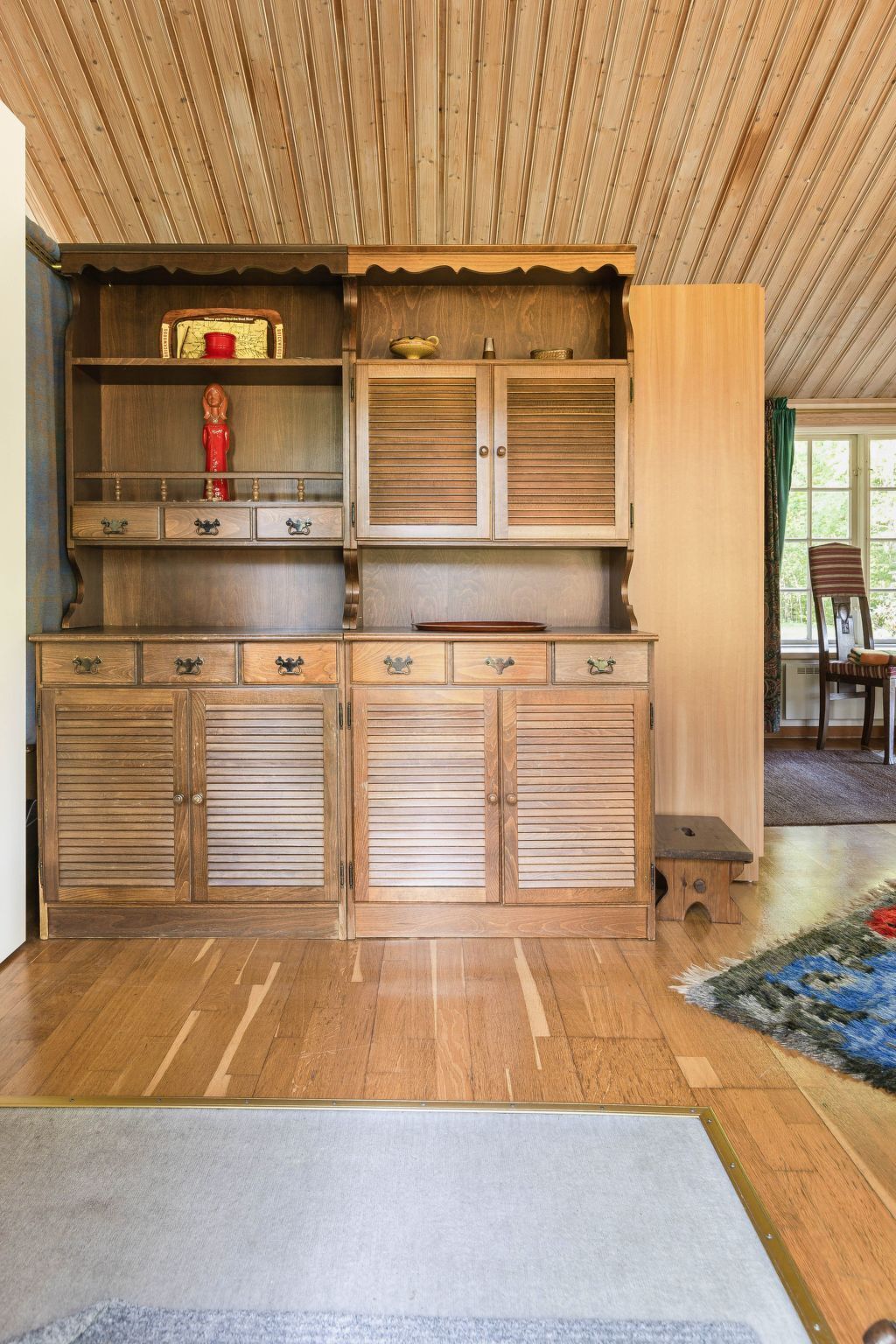 Ein Holzkabinent mit mehreren Schubladen und Regalen, ein kleiner Tisch und ein Stuhl in einem Zimmer mit Holzboden und einem Fenster.