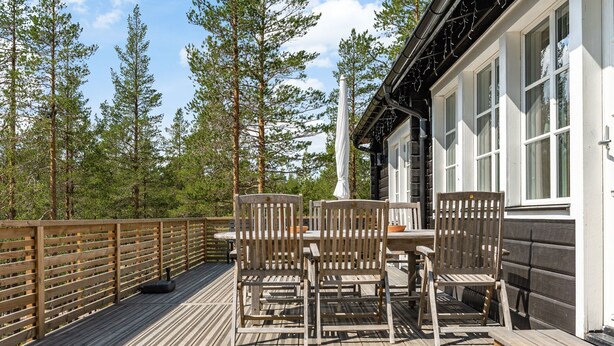 En træterrasse med et bord og stole, omgivet af et træhegn og høje træer.