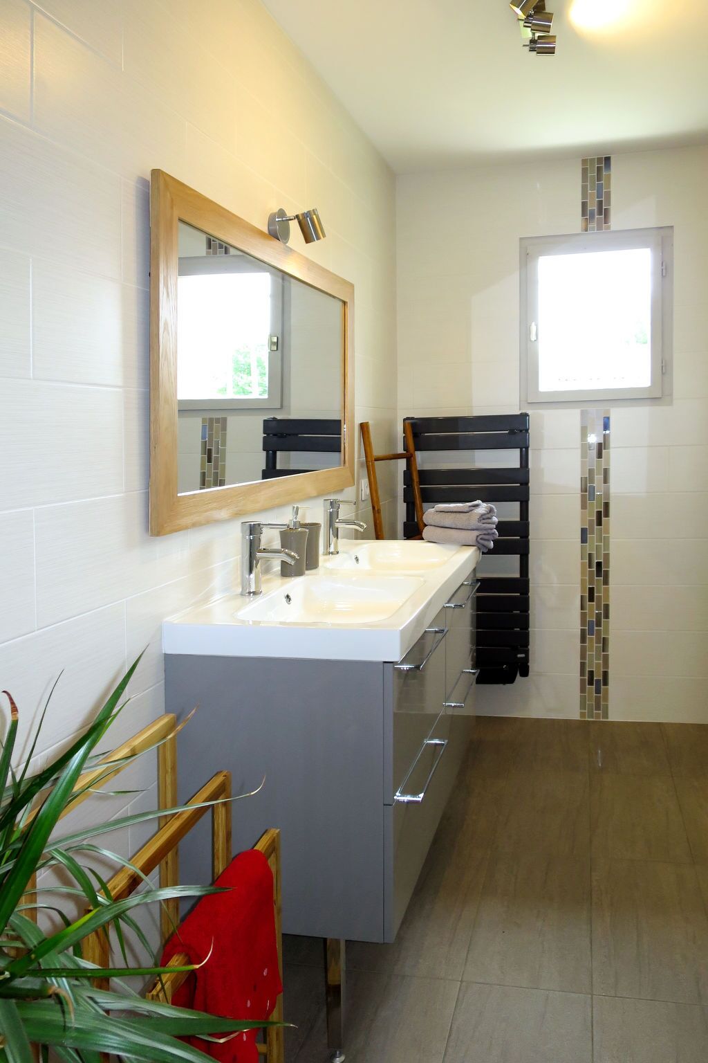 A modern bathroom with a large mirror, two sinks, a towel rack, and a window.
