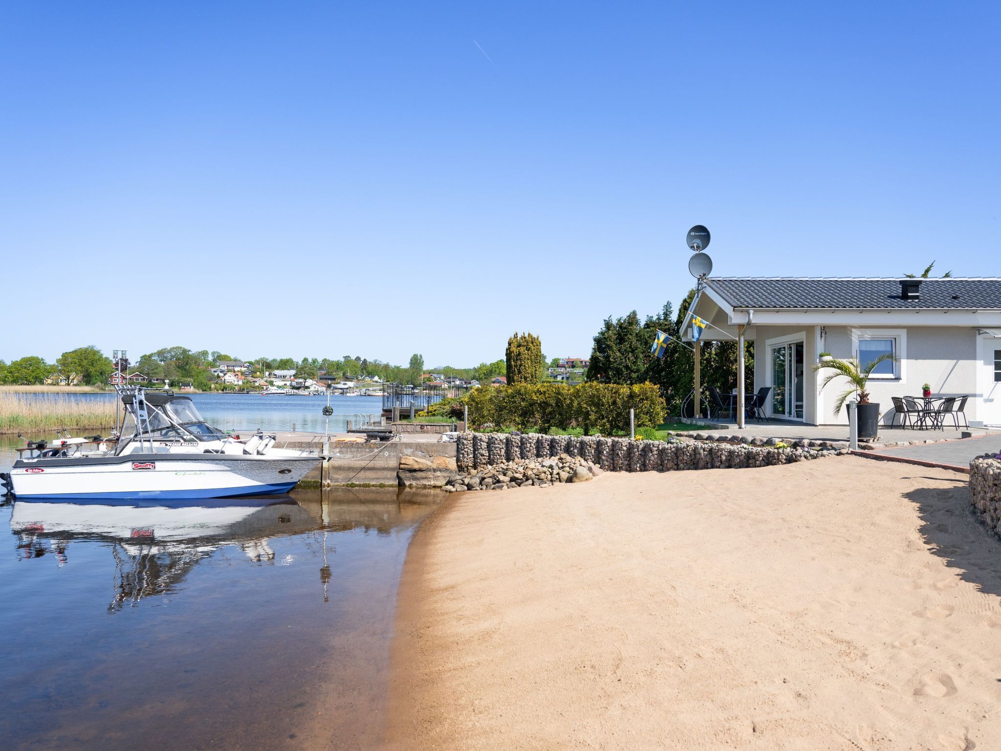 A sandy beach with a boat docked near a house with a satellite dish.