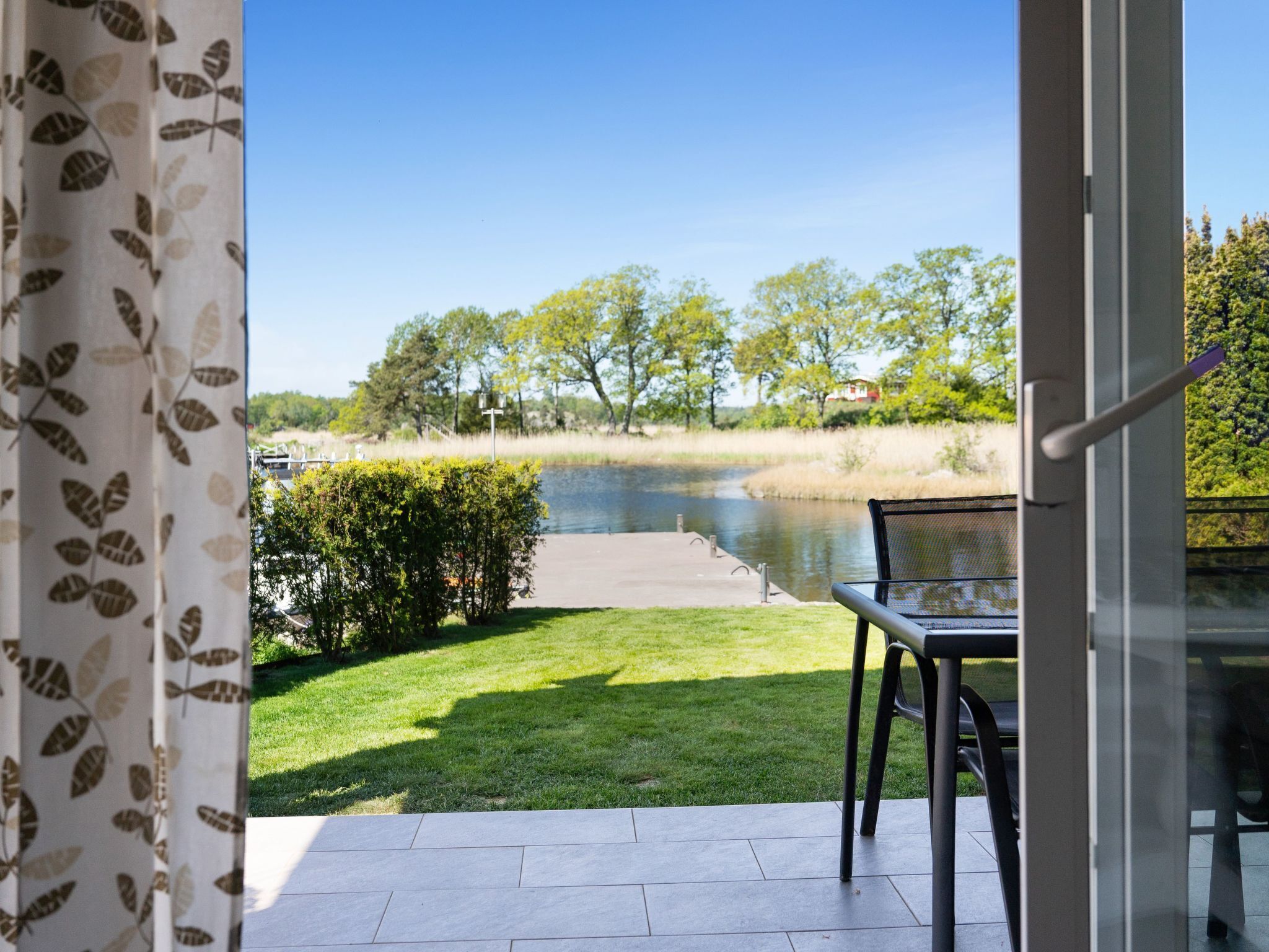 A patio with a view of a river, a grassy area, and a chair.