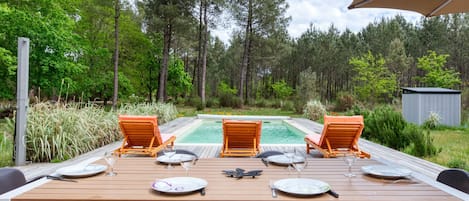A wooden deck with a pool, surrounded by tall trees and a small shed.