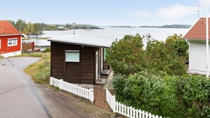 Une petite cabane en bois avec une clôture blanche en piquets, un bâtiment rouge et une vue sur un lac.