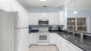 Una cocina moderna con armarios blancos, un refrigerador de acero inoxidable, un microondas y una estufa.
